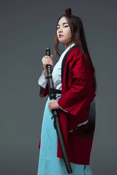 Beautiful asian woman in kimono holding katana and looking at camera isolated on grey — Stock Photo