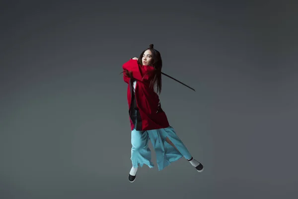 Молодая женщина в кимоно, дерущаяся с Катаной в прыжке изолированная на сером — стоковое фото
