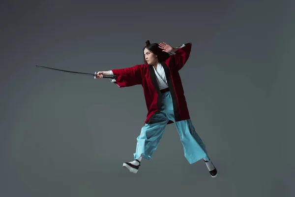 Full length view of samurai in kimono fighting with katana in jump isolated on grey — Stock Photo