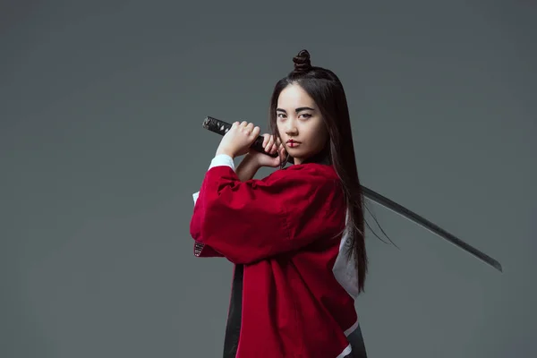 Young woman in kimono holding katana and looking at camera isolated on grey — Stock Photo