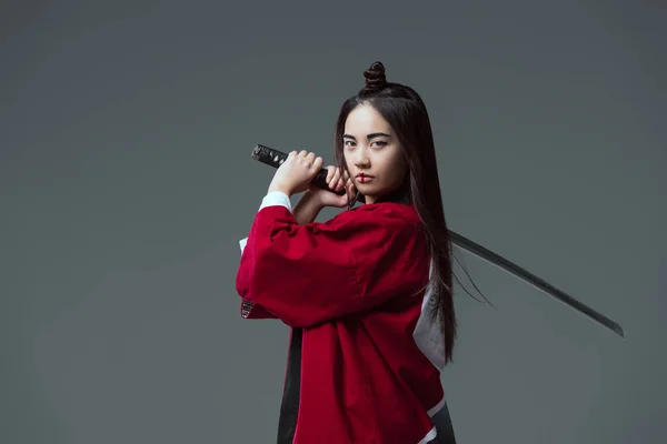 Mujer joven en kimono sosteniendo katana y mirando a la cámara aislada en gris - foto de stock