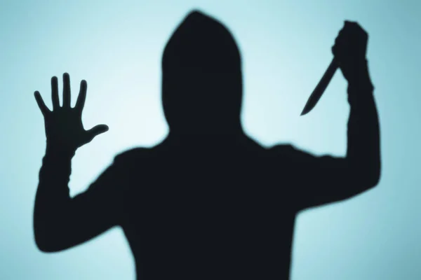 Sombra assustadora de pessoa no capuz segurando faca no azul — Fotografia de Stock