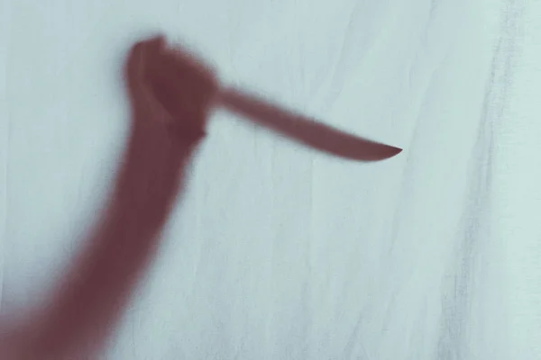 Scary blurry silhouette of person holding knife behind veil — Stock Photo