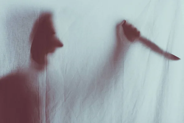 Scary blurry silhouette of person screaming and holding knife behind veil — Stock Photo