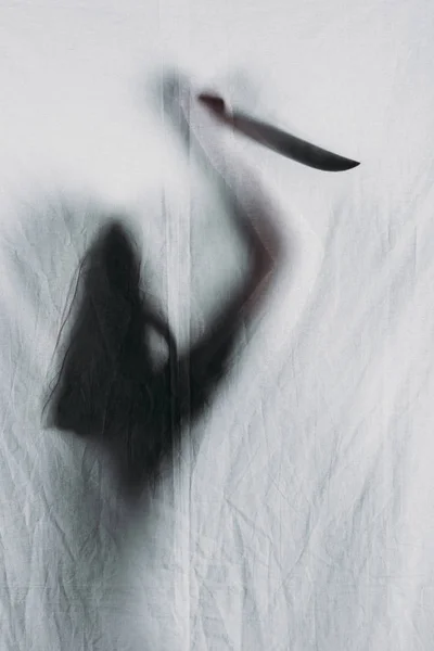 Scary blurry silhouette of person holding knife behind veil — Stock Photo