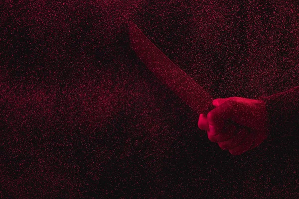 Recortado tiro de hombre sosteniendo cuchillo en luz roja con fallos - foto de stock