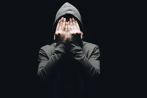 Cropped shot of man in hoodie closing eyes with hands isolated on black — Stock Photo