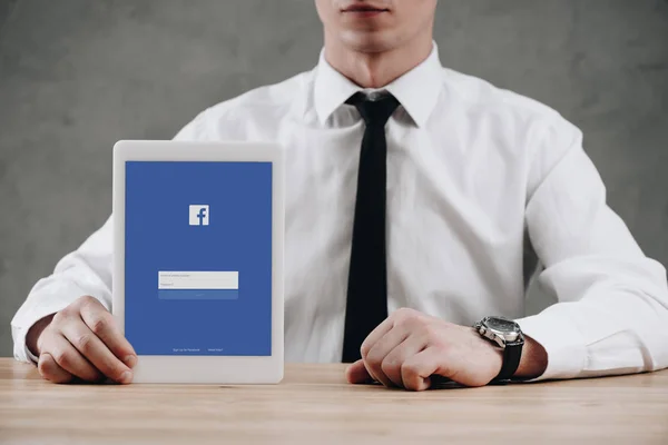 Mittelteil des Geschäftsmannes hält digitales Tablet mit Facebook-Website auf dem Bildschirm — Stockfoto
