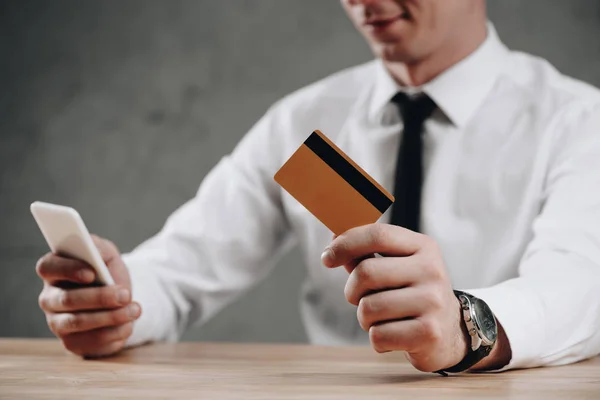 Tiro recortado de empresário segurando cartão de crédito e usando smartphone — Fotografia de Stock