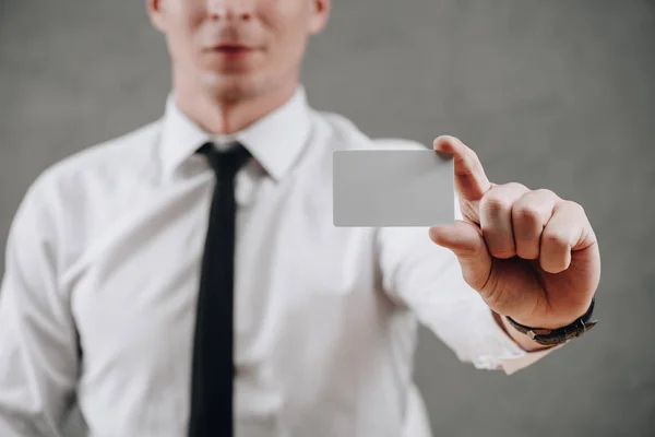 Tiro recortado de empresário segurando cartão em branco no cinza — Fotografia de Stock