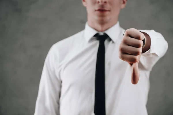 Recortado tiro de hombre de negocios mostrando pulgar hacia abajo en gris - foto de stock