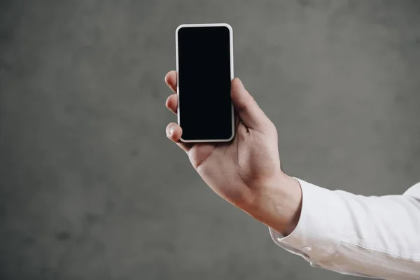 Tiro recortado de homem segurando smartphone com tela em branco no cinza — Fotografia de Stock