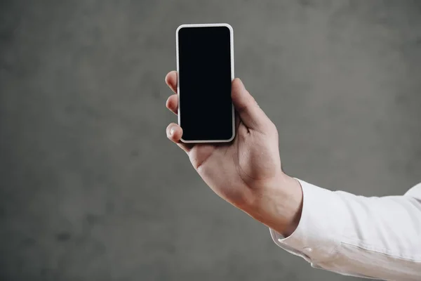 Cropped shot of man holding smartphone with blank screen on grey — Stock Photo