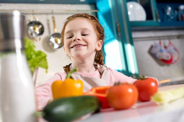 Очаровательный маленький ребенок улыбается во время приготовления пищи на кухне — стоковое фото