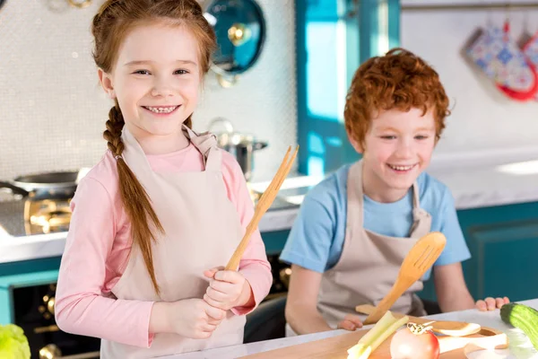 Entzückende Kinder in Schürzen lachen beim gemeinsamen Kochen in der Küche — Stockfoto