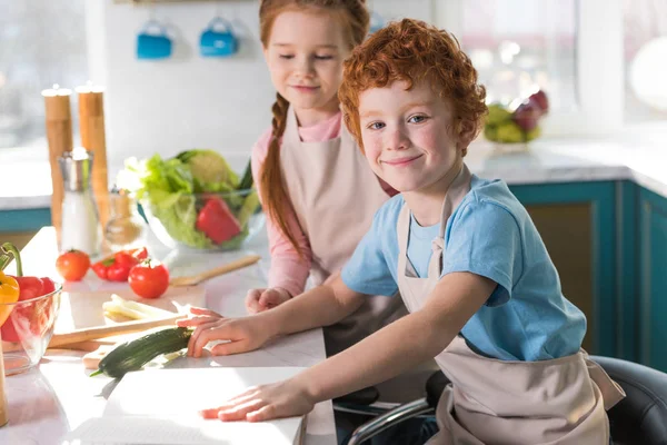 Bellissimi bambini felici in grembiuli che cucinano insieme in cucina — Foto stock