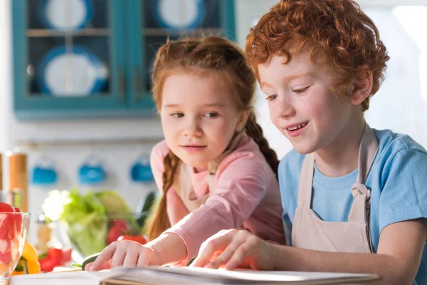 Adorable children reading cookbook while cooking together in kitchen — Stock Photo