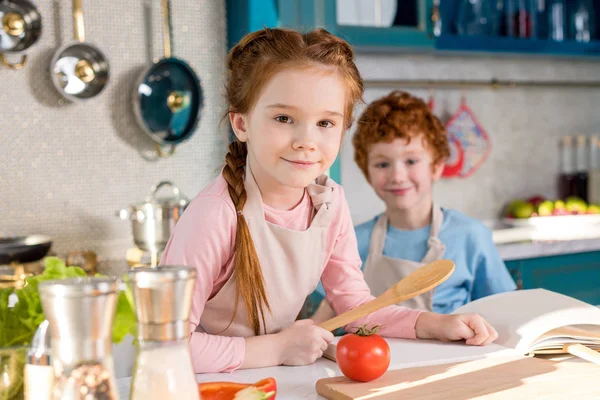 Adorabili bambini sorridenti alla macchina fotografica mentre cucinano insieme in cucina — Foto stock