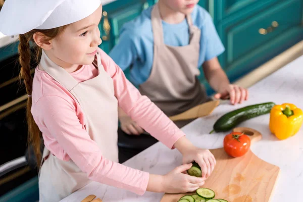 Schnappschuss von niedlichen kleinen Kindern in Schürzen, die gemeinsam in der Küche Gemüsesalat kochen — Stockfoto