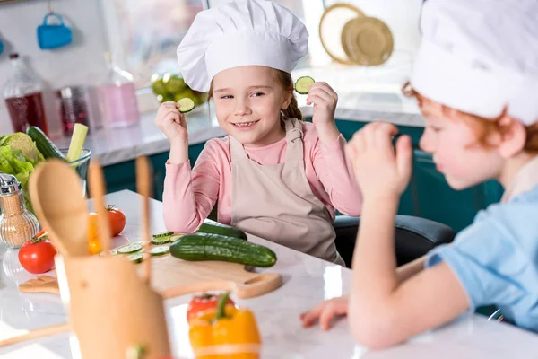 Милые маленькие дети в шляпах шеф-повара веселятся во время приготовления пищи вместе на кухне — стоковое фото
