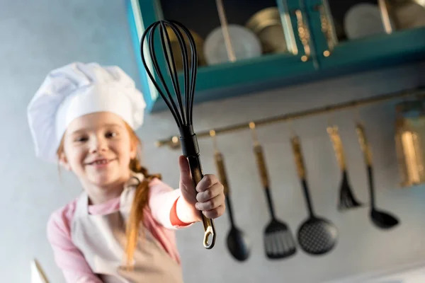 Vista de cerca de niño sonriente en sombrero de chef con batidor en la cocina - foto de stock