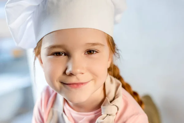 Adorable niño en sombrero de chef sonriendo a la cámara - foto de stock