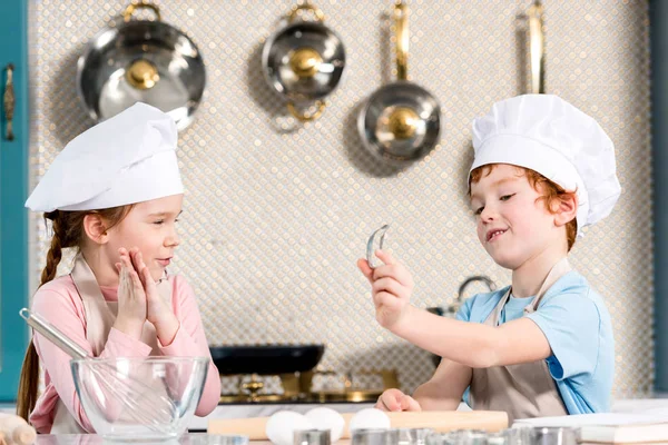 Очаровательные дети в шляпах шеф-повара и фартуках готовят вместе на кухне — стоковое фото