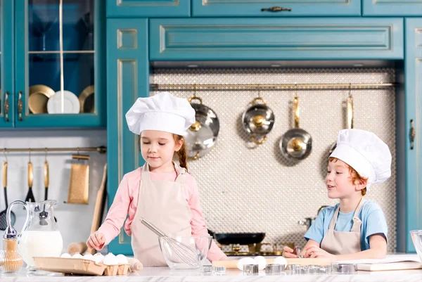 Niños con gorras y delantales cocinando juntos en la cocina - foto de stock