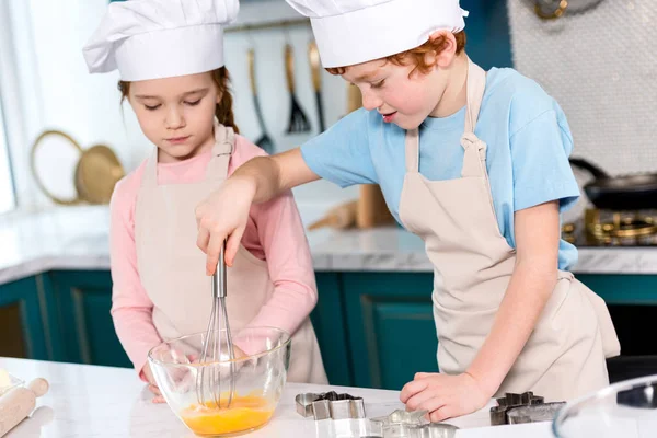 Geschwister in Kochmützen und Schürzen, die Teig in der Küche verquirlen — Stockfoto