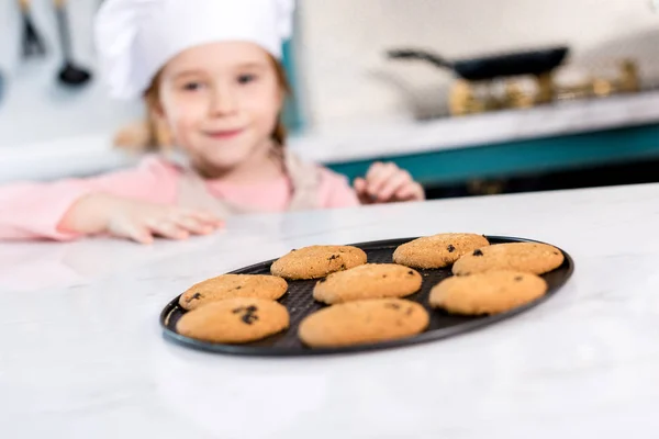 Primer plano vista de sabrosas galletas dulces y niño en sombrero de chef detrás - foto de stock