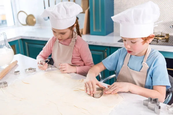 Adorabili bambini in cuoco cappelli e grembiuli preparare i biscotti insieme — Foto stock