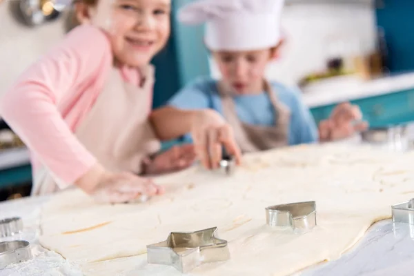 Vista de cerca de masa sin cocer y formas para galletas y niños pequeños y lindos en la cocina - foto de stock