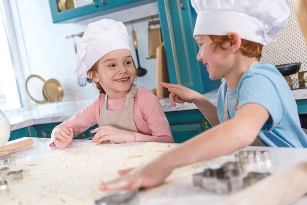 Милые маленькие дети улыбаются друг другу во время приготовления печенья вместе — стоковое фото