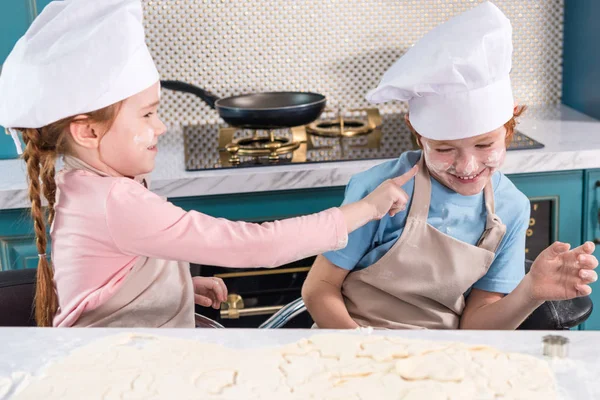 Crianças bonitos em chapéus de chef se divertindo com farinha na cozinha — Fotografia de Stock