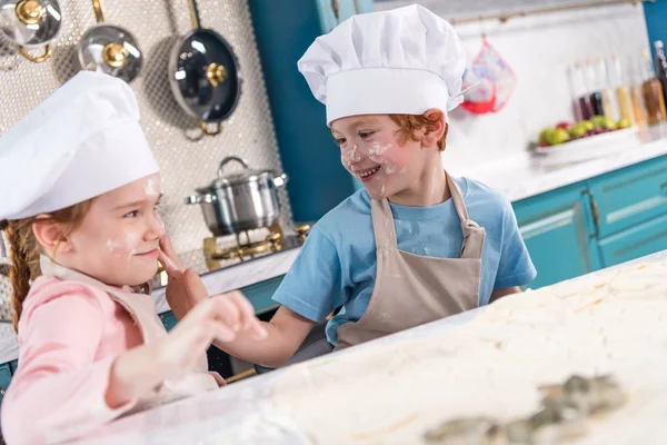 Crianças bonitos em chapéus chef se divertindo com farinha na cozinha — Fotografia de Stock