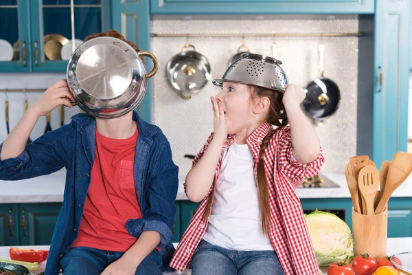 Entzückende kleine Kinder, die sich am Küchentisch mit Utensilien vergnügen — Stockfoto