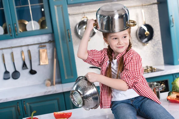 Cute little child having fun with utensils while sitting on kitchen table — Stock Photo