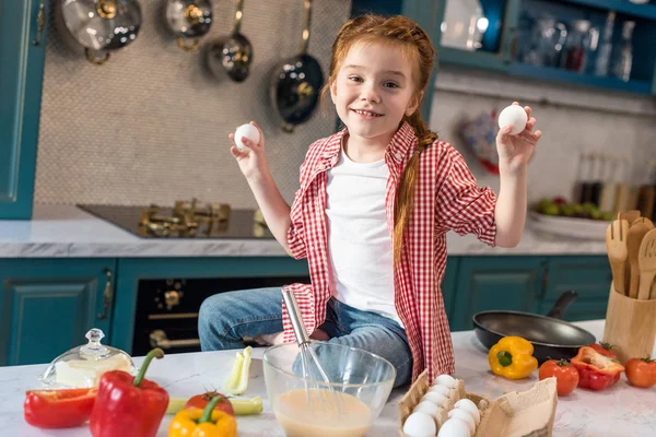 Carino bambino che tiene le uova e sorride alla fotocamera in cucina — Foto stock