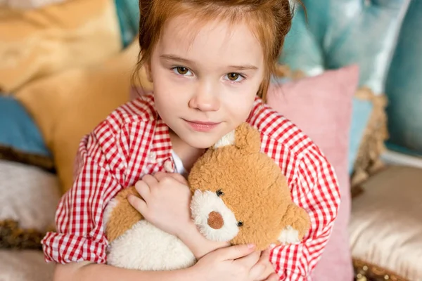 Lindo niño pequeño abrazando osito de peluche y sonriendo a la cámara - foto de stock