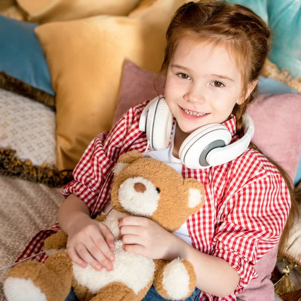 Mignon petit enfant dans casque tenant ours en peluche et souriant à la caméra — Photo de stock