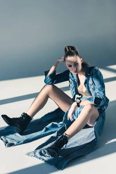 Beautiful young woman in denim clothes sitting on floor with shadows — Stock Photo