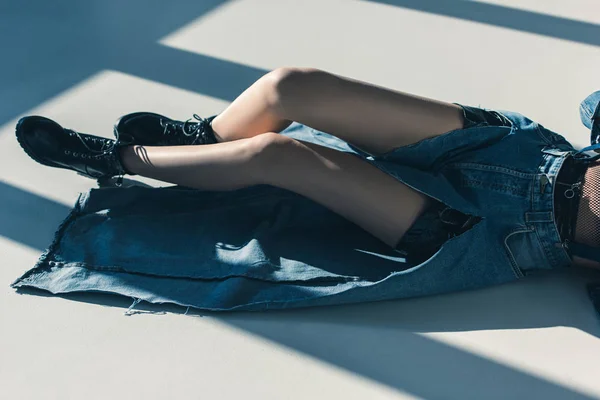 Обрезанный вид девушки в джинсовой одежде лежащей на полу с тенями — стоковое фото