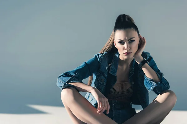 Привлекательная девушка в джинсовой одежде сидит на полу с тенями — стоковое фото