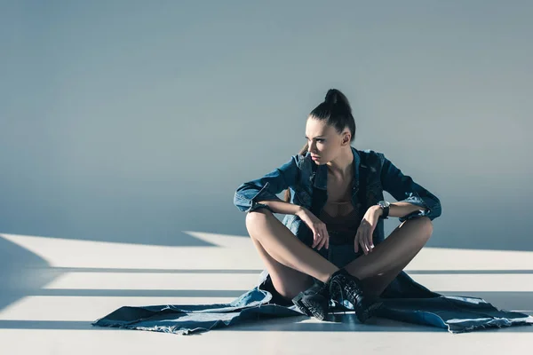 Chica atractiva en ropa de mezclilla sentado en el suelo con sombras - foto de stock