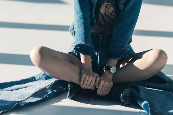 Обрезанный вид женщины в джинсовой одежде, сидящей на полу с тенями — стоковое фото