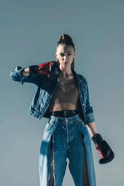 Chica con estilo en ropa de mezclilla posando con guantes de boxeo, aislado en gris - foto de stock