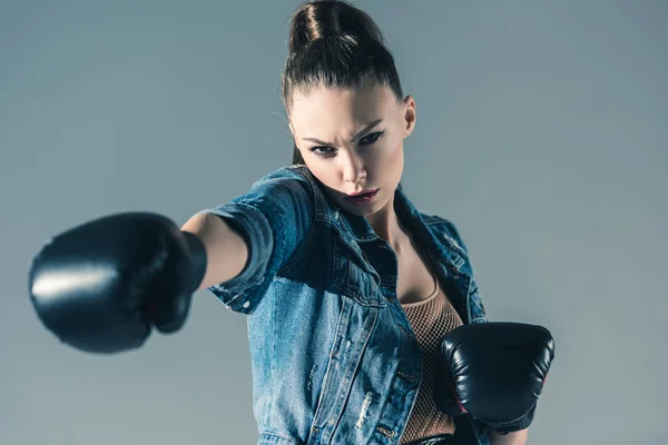 Caucasian girl in denim clothes and boxing gloves, isolated on grey — Stock Photo