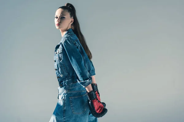 Stylish brunette girl in denim clothes and boxing gloves, isolated on grey — Stock Photo
