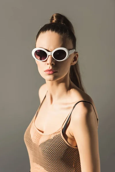 Fille élégante avec une coiffure en queue de cheval dans les lunettes de soleil, isolé sur gris — Photo de stock