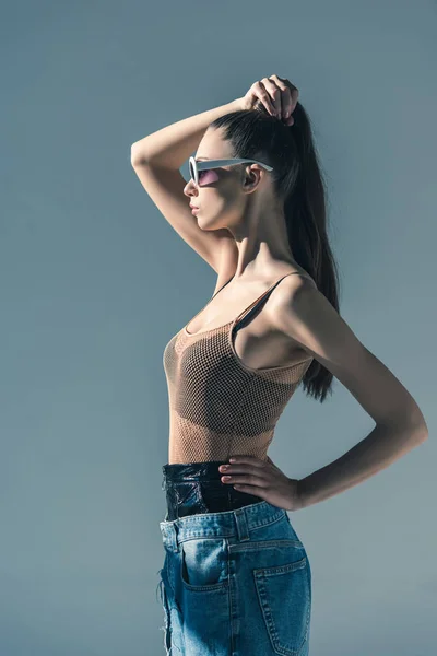 Красивая девушка позирует в солнцезащитных очках с прической из хвостика, изолированная на сером — стоковое фото